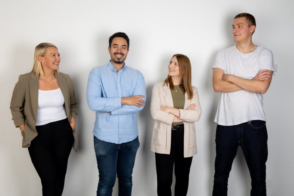 Teamfoto mit vier Mitarbeitenden vor heller Wand