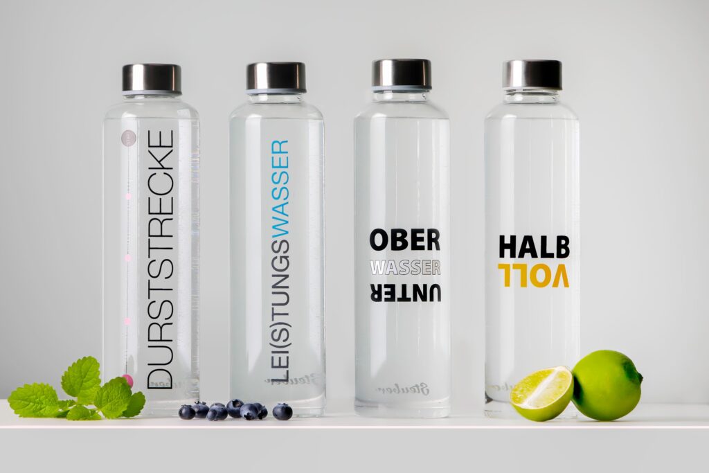 Vier bedruckte Glasflaschen mit Limette und Minze